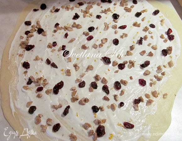 Поднявшееся тесто разделить на 2 части для удобной работы. Раскатать одну часть, не очень тонко. Смазать белком, оставляя по краю место в 1-2 см.
Посыпать клюквой и орехами. Свернуть рулетом.