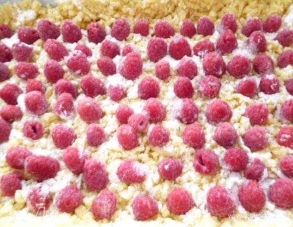 Форму для выпечки застелить пергаментом,смазать маргарином и присыпать манкой.Достать тесто из холодильника.Отделить часть теста величиной с яйцо и убрать в морозилку.Остальное тесто натереть через крупную терку и равномерно распределить по форме,сформовать бортик.Через ситечко тесто слегка подпылить крахмалом.Распределить малину(в моем случае замороженная)