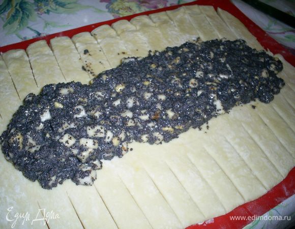 Готовое тесто делим на две части, каждую раскатываем в прямоугольный пласт толщиной меньше сантиметра. По краям пласта острым ножом делаем надрезы шириной около 1,5 см и длинной 7-8 см. На средину каждого пласта выкладываем половину начинки.