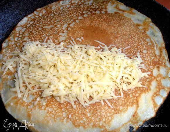 Когда с одной стороны блинчик позолотится, переворачиваем и скорей насыпаем столовую ложку сыра на одну половинку блина.