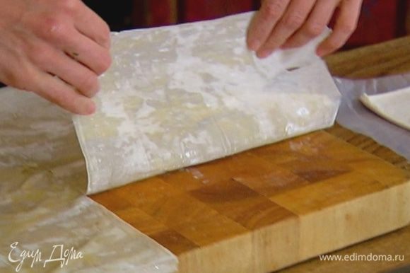 Лист теста фило смазать растопленным маслом, выложить на него второй лист и также промазать маслом, затем разрезать тесто на две части, каждую часть сложить пополам.