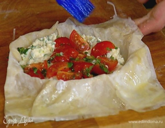 Выложить в центр каждой формы творожную начинку, а сверху помидоры с базиликом, промазать сливочным маслом свисающее тесто и загнуть его внутрь по краям тартов, так чтобы начинка в центре осталась открытой.