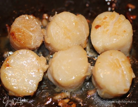 На оливковом масле обжарить чеснок, добавить морские гребешки и обжарить их по 1 минуте с каждой стороны. Влить вино и прогреть еще 2 минуты. Выложить гребешки в слоеные формочки и накрыть "крышками"