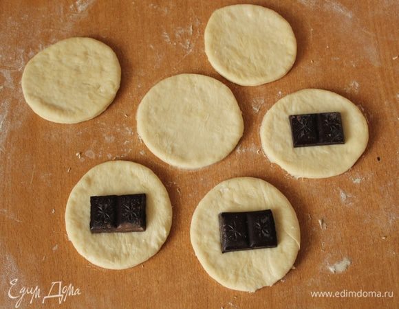 В центр одного кружка положить кусочек шоколада, накрыть вторым и хорошо прижать края. Края предварительно смазать водой.