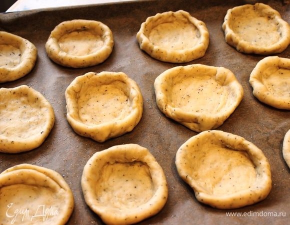 Разделить тесто на шарики...каждый немного раскатать или растянуть руками....в центре лепешки сделать углубление пальчиками, чтобы приподнять бортики ватрушки. Выложить заготовки на противень, застеленный бумагой