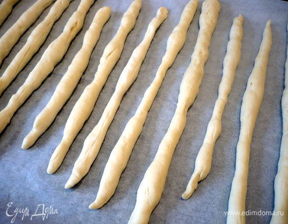 Каждую часть раскатываем в тонкую колбаску длиной 20 см (у меня получилось подлинней, просто, чем тоньше получаются гриссини, тем они хрустящей). Оставляем на 15 минут под полотенцем. Духовку разогреваем до 220 градусов с конвектором. Смазываем каждую палочку водой и посыпаем розмарином и кунжутом. 
