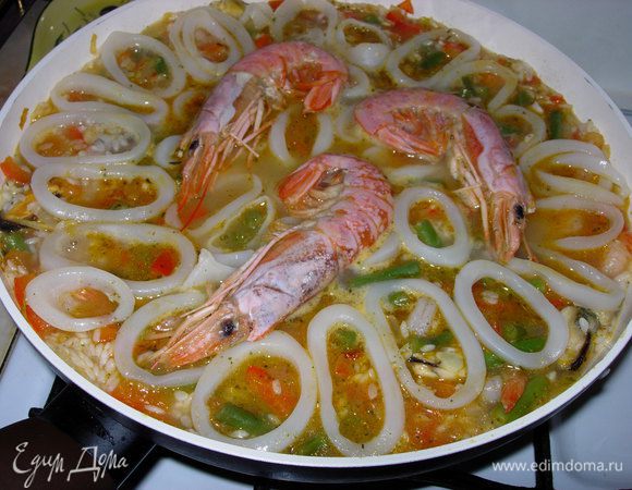 Выкладываем мясо кальмара, порезанного кольцами и тигровые креветки. Оставляем паэлью на плите. Готовность блюда легко определить по рису, напитавшемуся бульоном. Потребуется примерно 25-30 минут.