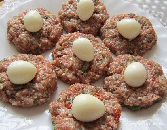 Из фарша сформировать небольшие лепёшечки, в центр каждой положить перепелиное яйцо, соединить края и скатать шарик.