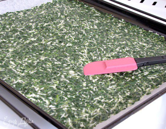 Отправьте шпинатную смесь на противень, застеленный пекарской бумагой и хорошо разровняйте лопаткой.