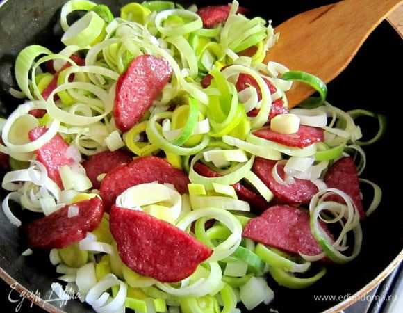 Разогреть в сковороде 2 ст. л. оливкового масла, обжарить колбасу в течение 5 мин. Добавить репчатый лук и лук порей, обжарить в течение 7 мин.
