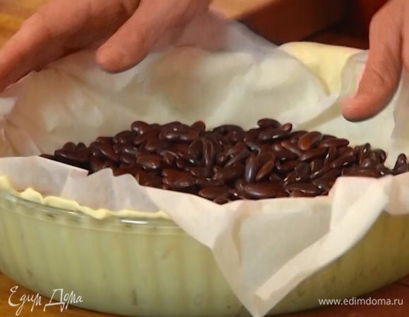 Поместить на тесто бумагу для выпечки, насыпать сверху фасоль или горох и отправить в разогретую духовку.