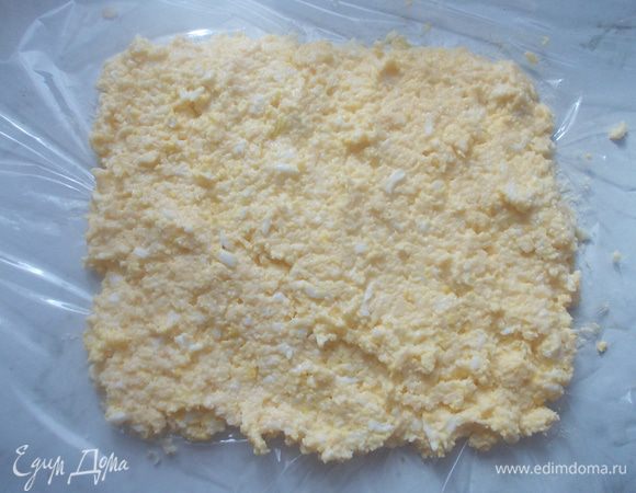 Потереть сыр, яйцо и чеснок на терке. Добавить немного майонеза, чтобы скрепить сыр. Выложить все на пищевую пленку и разровнять.