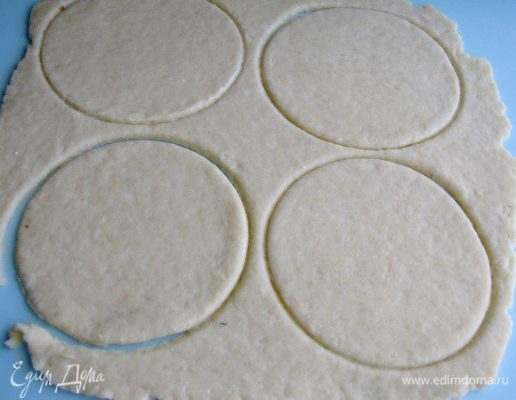 Достать тесто из холодильника, раскатать на присыпаной мукой поверхности в пласт, вырезать из него кружки. Диаметр кружков должен быть немного больше диаметра формочек.