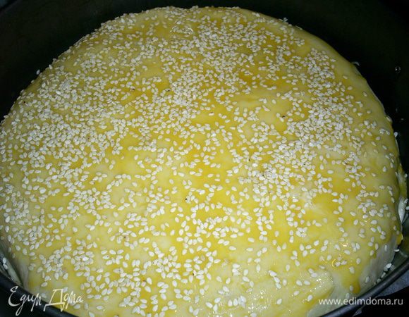 На бумаге или силиконовом коврике раскатываем оставшееся тесто в круг с диаметром большим диаметра сковороды. С помощью бумаги, коврика переносим тесто и укладываем его на начинку. Края круга подгибаем внутрь формы, закрывая начинку. Смазываем поверхность пирога желтком и посыпаем кунжутом. Часто накалываем вилкой. Отправляем пирог в разогретую до 180 градусов духовку на 35-40 минут. Следите, чтоб пирог не подгорел, но зарумянился.