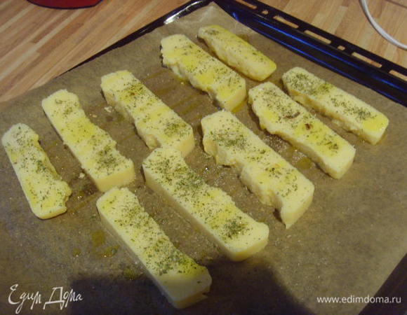 Загустевшую поленту порезать на бруски, выложить на противень, сбрызнуть оливковым маслом, посолить, поперчить, посыпать травками и запечь под грилем при 200° до золотистой корочки.