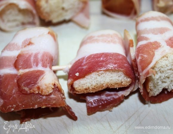 Ломтик багета разрезать на крупные кусочки (примерно 3 см диаметром), Каждый обернуть в тонкую пластинку бекона. насадить все кусочки на деревянную шпажку, оставляя между ними небольшое расстояние