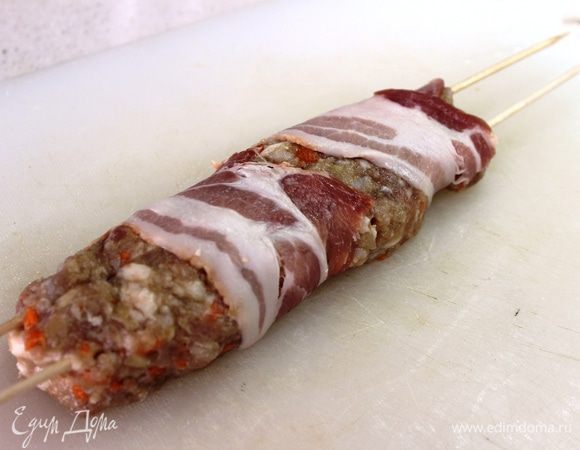 Свободный конец бекона надо обернуть вокруг колбаски (при этом можно пользоваться широким ножом, приподнимая им краешек колбаски, чтобы без проблем просунуть под нее бекон)