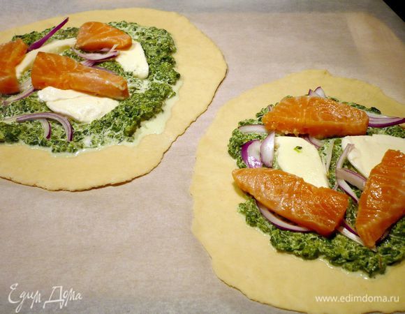 Каждый круг смазываем сметаной со шпинатом так, чтобы по краям пара сантиметров теста оставалась свободной. Выкладываем сверху полосочки лука, моцареллу и немного внахлест на моцареллу — семгу. Солим и перчим, посыпаем травами. Переносим в духовку прямо на бумаге по два круга и кладем на противень на 7 минут. Выпекаем до золотистой корочки по краям. 