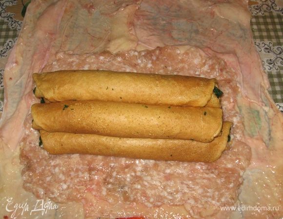 Теперь на стол выстилаем пищевую пленку с запасом со всех сторон (это для удобства и чистоты), поперек раскладываем жгуты из кулинарной нити для связывания и внахлест выкладываем из куриных шкурок четырехугольник. Поверх шкурок нужно также внахлест выложить отбитые кусочки куриной грудки или, как в моем случае, тонким слоем оставшийся куриный фарш. По центру экспозиции располагаем блинчики (2х2) и аккуратно, за пленку сворачиваем в рулет. Заворачиваем шкурку по бокам и перевязываем подготовленными нитками. Подтягиваем шкурку, если где слезла и подкалываем зубочистками.