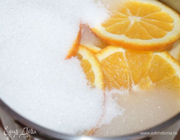 В кастрюлю выложить кружочки апельсинов, засыпать сахаром (350 г) и залить водой (400 мл).
Поставить на огонь, довести до кипения и варить на среднем огне под крышкой 20 минут. Остудить. Сироп не выливать.