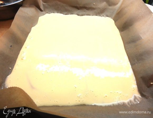 Вливаем молоко и вино, еще раз взбиваем. Затем вводим муку и разрыхлитель, взбиваем до однородности. Противень выстилаем бумагой для выпечки, слегка смазываем растительным маслом без запаха, равномерно распределяем по нему тесто тонким слоем.