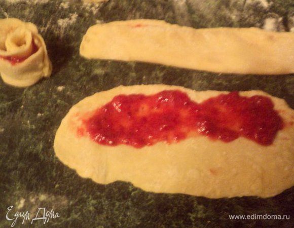 Из теста скатать валик и разрезать его на небольшие кусочки. Каждый кусочек раскатать в удлиненный овал, одну половинку смазать начинкой. Сложить тесто пополам, краешки по бокам немного защипнут, чтобы не вытекала начинка. Свернут получившуюся полоску улиткой, край защипнуть, чтобы не разворачивалась. Краешки разровнять в виде розочки.