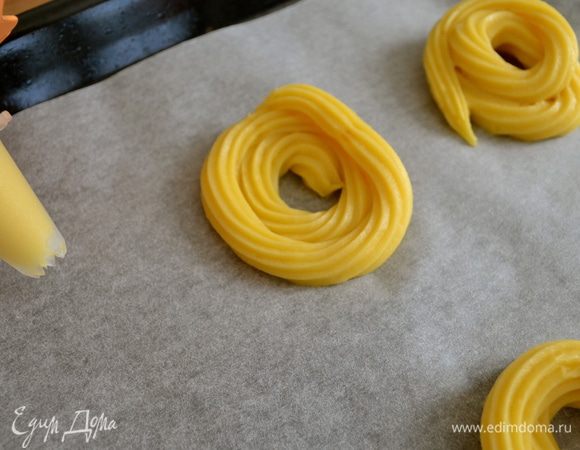 Духовку разогреть до 200 С. Противень застелить пекарской бумагой. Переложить тесто  в кондитерский мешок и с помощью фигурной насадки выложить на противень маленькие пончики в форму бубликов, крендельков... Полосочку теста заворачиваем по кругу в два ряда! Как на фото....