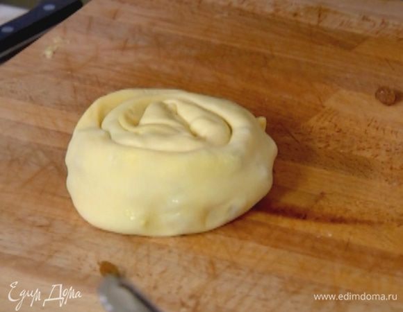 Пласт теста разрезать пополам, одну часть смазать яичным кремом, посыпать изюмом и свернуть в рулет, затем скрутить улиткой.