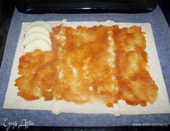 Слоеное тесто разморозить при комнатной температуре.
Яблоки очистить от кожуры, и удалить сердцевину. Нарезать на восьмушки.

Тесто выкладываем на пергамент, и слегка раскатываем до формы противня. Острым ножом, отступив от края теста 3 см, по всему периметру делаем прорезь, но не до конца, для того чтобы при выпечке поднялись края пирога.

Размазываем яблочное повидло по тесту и раскладываем яблоки, посыпаем корицей.
