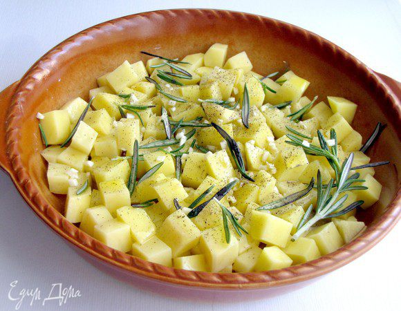 Разогрейте духовку до 200 гр. Картофель нарежьте на кубики, размером примерно 2 см и выложите в форму для запекания. Полейте картофель оливковым маслом, посыпьте измельченным чесноком и розмарином, посолите, поперчите. Хорошо перемешайте. Запекайте картофель 25-30 минут до готовности, пока корочка не станет золотистой и хрустящей.