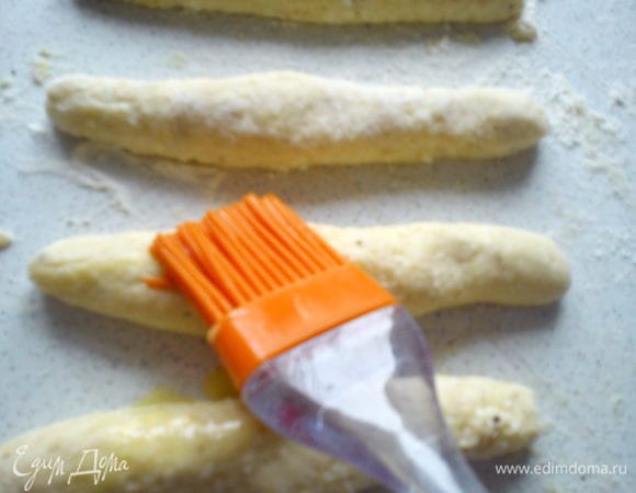 Скатать каждый кусочек в колбаску, при этом концы должны быть тоньше середины. Смазать желтком поверхность колбасок