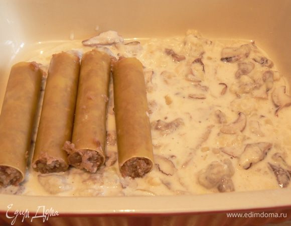 Часть соуса налить в форму, уложить начиненные фаршем каннелони.