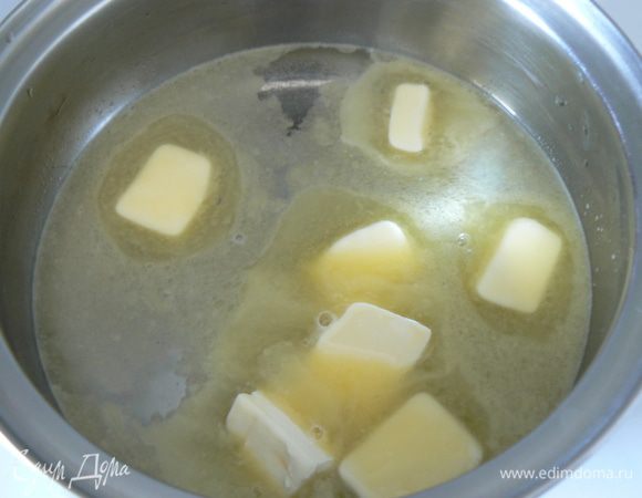 В чашку налить воду, добавить кусочки масла и поставить на умеренный огонь. Помешивать, пока масло полностью не растает