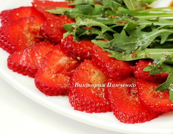Выложить на плоское блюдо ломтики клубники внахлест, сверху положить руколу, всё обильно полить пряной заправкой и подавать немедленно.