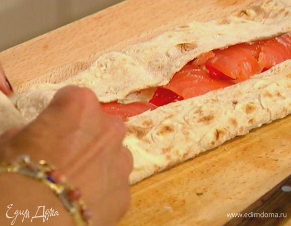 Лаваш смазать сырной начинкой, равномерно разложить полоски сладкого перца и кусочки семги, подвернуть края, затем все скатать в рулет.