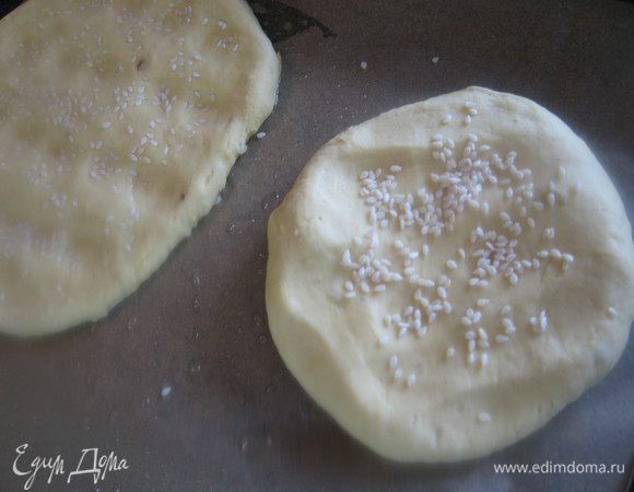 Делим тесто на 6-8 частей, это в зависимости какого размера лепешки вы предпочитаете. Я делала средние. Притивни застилаем бумагой, смазываем маслом и прямо на бумаге пальчиками аккуратно разминаем  лепешки. Посыпаем кунжутом и легонько вдавливаем  его в тесто.  