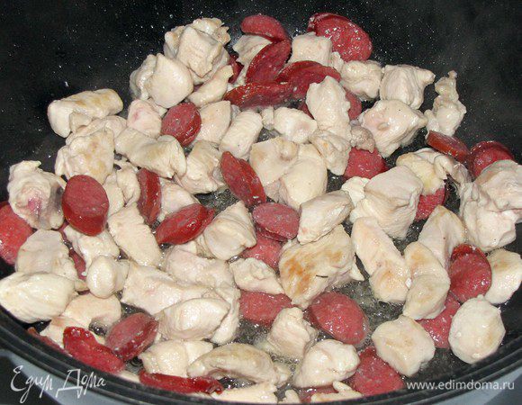 Разогреть в сотейнике растительное масло и обжарить в нем кусочки курицы и колбасок, 5 минут.