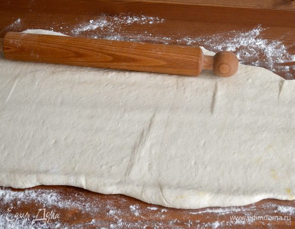 Как только тесто поднялось, присыпать мукой рабочую поверхность и раскатать его в пласт (приблизительно 40 Х 65 см). Отрезать от него полоску теста примерно 5 см, оно нам пригодится в дальнейшем для украшения. Завернуть отрезанный кусочек теста в пищевую пленку.