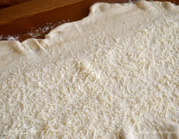 На раскатанное тесто выложить тертый сыр (оба вида).