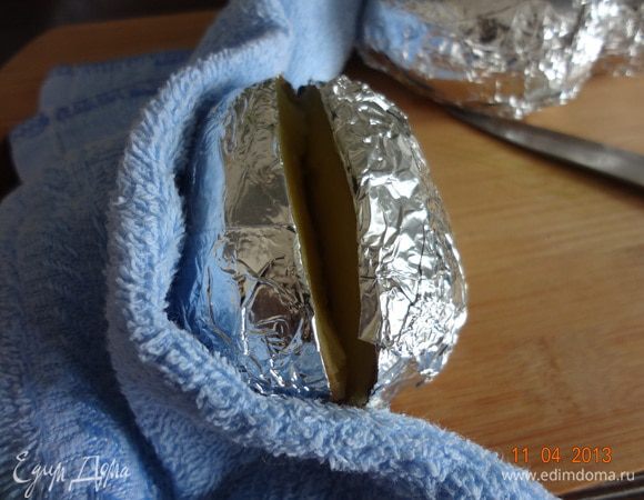 По истечение часа картофель достать из духовки очень осторожно, используя полотенце или прихватку. Выложить на разделочную доску, горячий картофель, придерживая полотенцем, надрезать вдоль, не до конца.