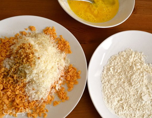 Далее, по классической итальянской "схеме" подготовки панировки для отбивных возьмем три тарелки. В одну насыпем муки, во вторую разобьем два яйца и размешаем их вилкой. В третью насыпем кукурузную крошку, к которой добавим хлопья сушеного лука (если Вы найдете эту специю, которая как нельзя лучше подходит к этому блюду!...), тертый твердый сыр и соль. (Обычно в третью емкость вместо кукурузных хлопьев насыпают панировочные сухари...)  
