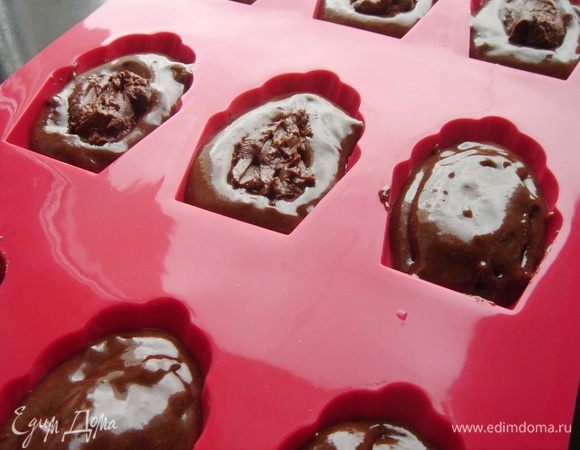 Форму для "Мадлен" смазать маслом и посыпать какао. Эта обязательная операция даже для силиконовых форм! Я понадеялась, что новая силиконовая форма не требует к себе такого внимания и именно поэтому мои "ракушки" потеряли свою форму. Каждую ракушку заполнить на половину тестом,затем добавить по половине чайной ложки ганаша и ещё чуть теста выложить на ганаш. Особенно не старайтесь спрятать начинку. Она "спрячется" при выпечке в поднявшемся тесте.