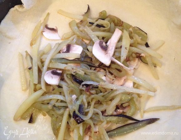 Положить один раскатанный  пласт теста на посыпанный мукой противень и выложить на его середину половину всех овощей (т.к. ингредиенты рассчитаны на два мини пирога) так, чтобы края теста оставались свободными