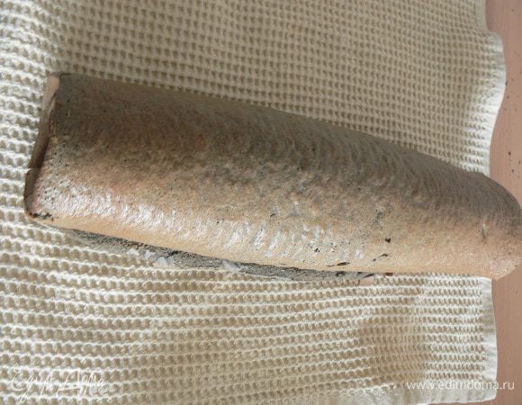 Готовый рулет вместе с бумагой снимаем с противня. Перевернуть пласт на полотенце, аккуратно снимаем бумагу. Теперь сворачиваем бисквитный пласт в рулет с помощью полотенца  и оставляем его в таком виде (завернутом) до полного остывания. 