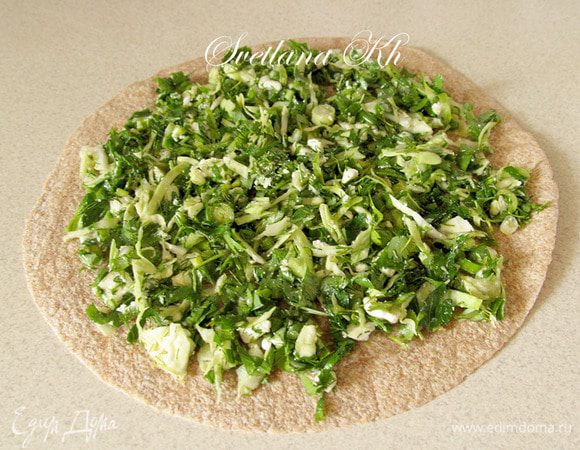 На лавашевую лепешку выложить начинку. Распределить по всей поверхности. Края смочить водой.