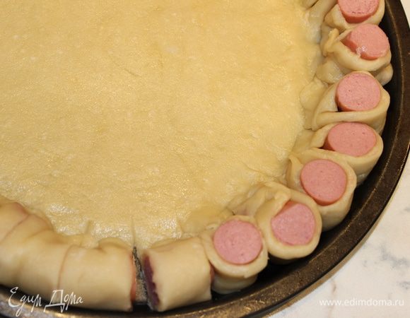 Надрезать сосиски и края теста насквозь, разделив каждую из них на 4 части (по всей длине окружности). Каждый надрезанный сегмент повернуть на 90 градусов так, чтобы сосиска оказалась сверху