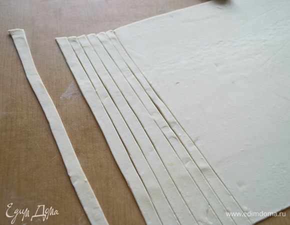 Готовое слоеное тесто разморозить и тонко раскатать, после чего нарезать длинными полосками шириной примерно 1 см.