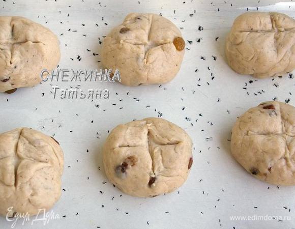 Делим тесто на 12 равных частей и формируем круглые булочки. Кладём их на смазанный противень и немного прижимаем сверху, чтобы они стали плоские. Делаем на них крестообразные надрезы ножом. Накрываем пищевой плёнкой и оставляем на 45 минут в тёплом месте, чтобы они увеличились вдвое.
