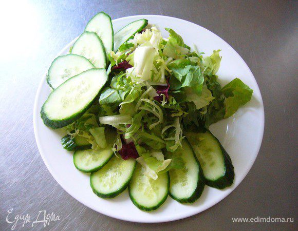 Нарезаем огурец тонкими пластинами по диагонали и выкладываем салат. Очень удачно выложить огурец веером, а сам салат горкой.