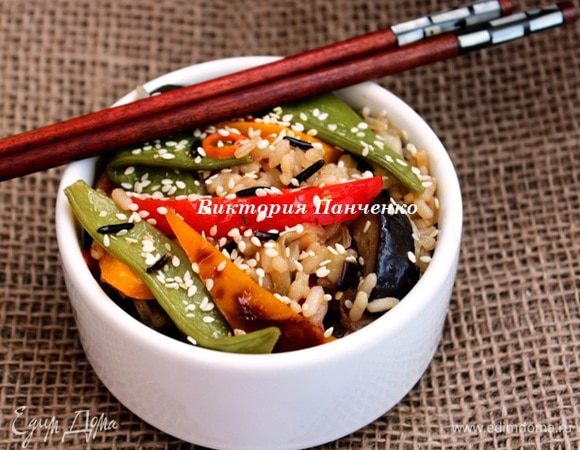 Лук, баклажаны и морковь обжарить на оливковом масле на сильном огне 2 минуты, добавить перцы и жарить еще 2 минуты, в последнюю очередь добавить зеленый горошек. Влить соевый соус и кунжутное масло, хорошо перемешать. Рис сварить до готовности. Добавить к овощам, перемешать, посыпать кунжутом и подавать немедленно